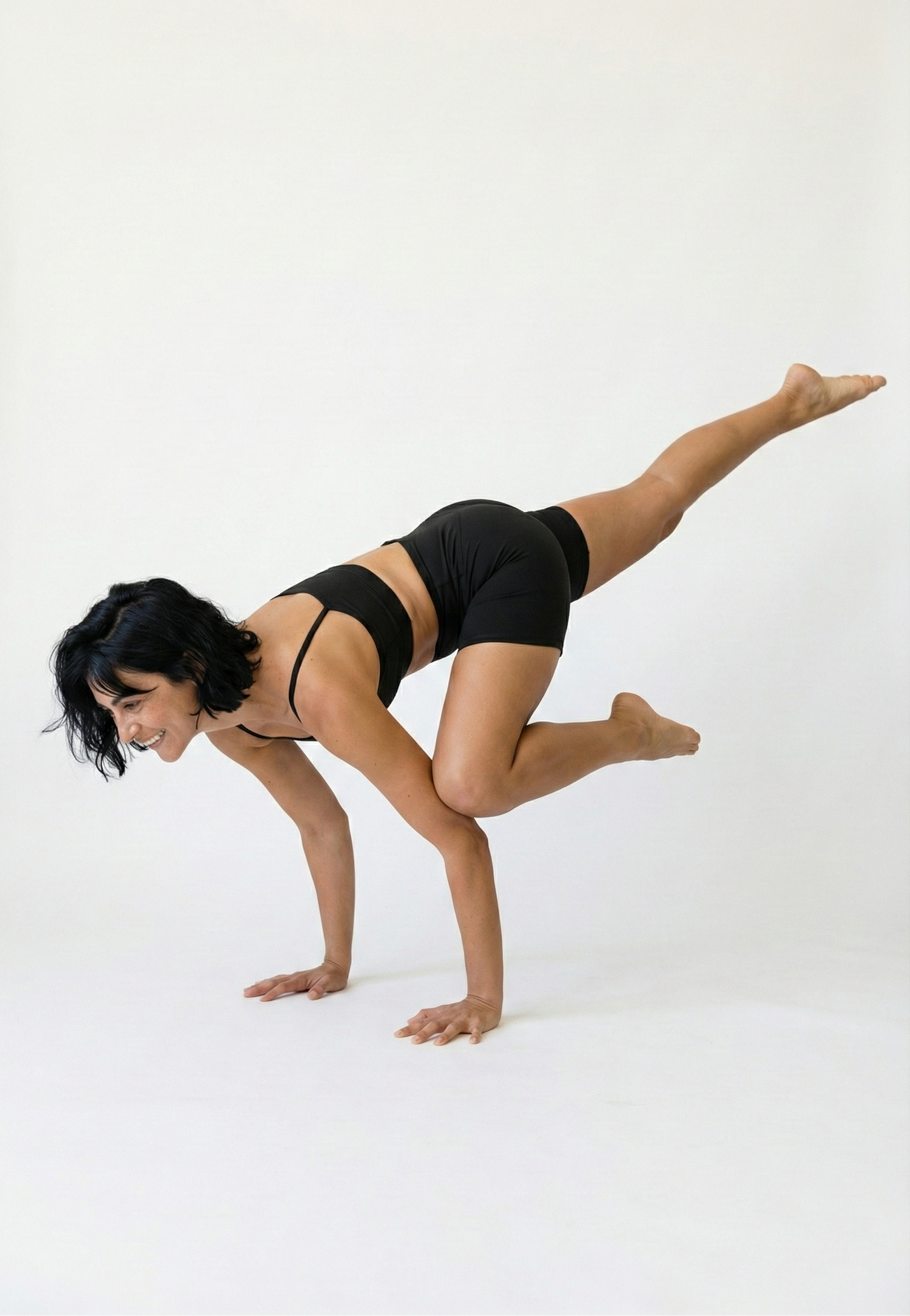 Person in a black sports bra and shorts performing a yoga pose on a white background